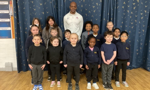 Olympian James Dasaolu stood smiling with pupils from EYFS and Year 6 of Nova Primary Academy. 